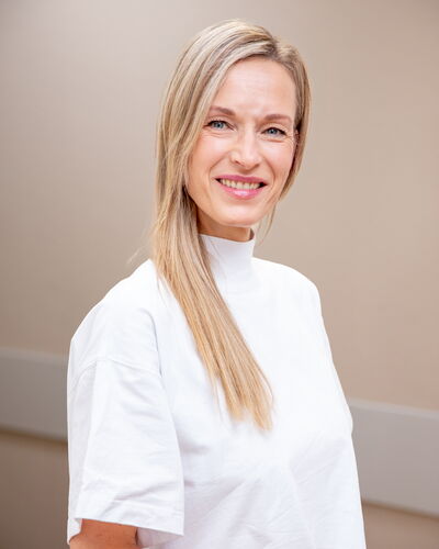 Anja Richter, Fachärztin für Innere Medizin und Nephrologie, steht in weißer Dienstkleidung vor einer neutralen Wand. Ihr freundliches Lächeln vermittelt medizinische Kompetenz und Empathie im Patientenkontakt.