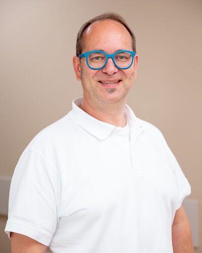 Dr. med. Andreas Sohn, Facharzt für Innere Medizin und Nephrologie, trägt ein weißes Poloshirt und blickt ruhig in die Kamera. Die dezente Umgebung lenkt den Fokus auf seine freundliche und kompetente Ausstrahlung.