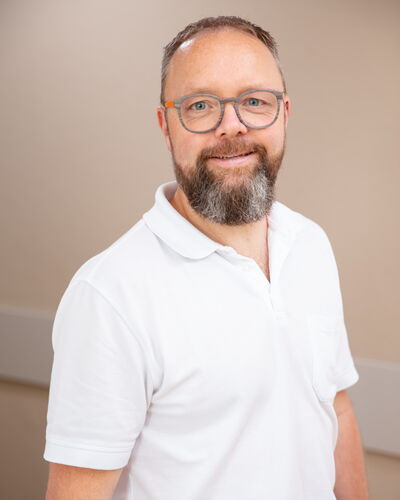 Dr. med. Markus Gläser, Facharzt für Innere Medizin und Nephrologie, steht entspannt vor einer beigen Wand. Sein Lächeln und die offene Körperhaltung spiegeln seine Zugewandtheit im ärztlichen Gespräch wider.