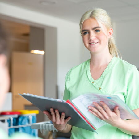 Eine Mitarbeiterin des Dialysezentrums ist im Gespräch mit einer Patienten. Sie hält eine Krankenakte in der Hand und schaut freundlich.