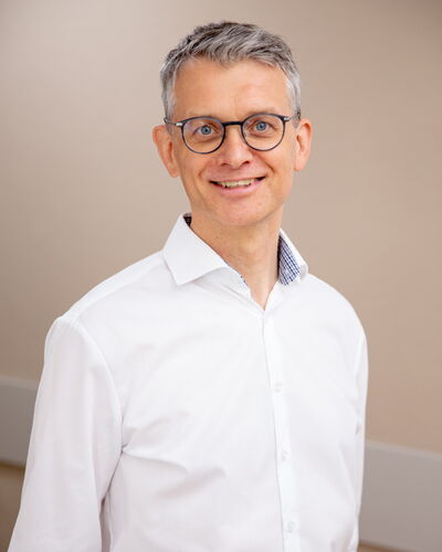 Dr. med. Jörg Schwöbel, Facharzt für Innere Medizin, Nephrologie und Diabetologie, steht lächelnd vor einer schlichten Wand. Sein professioneller Auftritt vermittelt Fachkompetenz und menschliche Nähe zugleich.